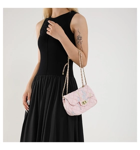 Detail of pink quilted crossbody bag with embroidery and gold chain on a black dress