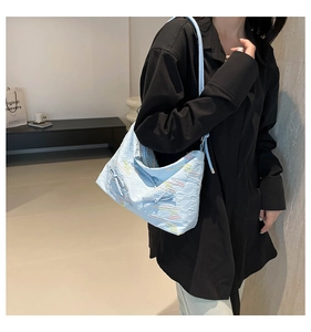 Detail of light blue embossed shoulder bag with colorful wavy embroidery and bow ornament