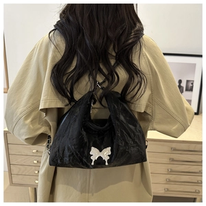 Détail du sac hobo noir avec emblème papillon argenté porté avec un trench-coat kaki élégant