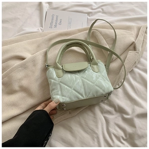 Detail view of mint green quilted crossbody bag with metal feet on textured fabric