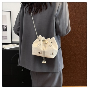 Cream drawstring bucket bag with silver butterfly studs and pearl accents on a model