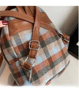 Detail of adjustable brown leather shoulder strap and silver metal buckle on plaid backpack
