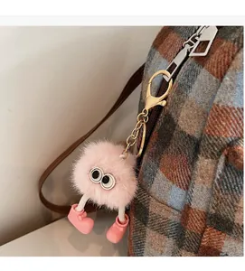Close-up of pink fluffy monster keychain with big eyes on a checkered backpack
