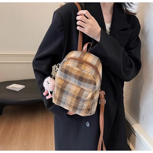 Detail view of a vintage plaid backpack with brown straps and a pink plush monster charm