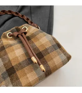 Détail du sac seau à cordon à carreaux montrant la texture du tweed et la lanière en cuir