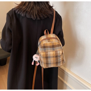 Detailed texture of mini checkered tweed backpack with a plush monster charm on the side