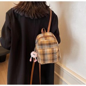 Details eines karierten Mini-Rucksacks mit Lederriemen und rosa Plüschanhänger-Deko