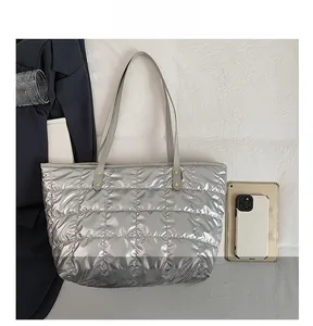 Detail view of silver quilted puffer tote bag compared with a tablet for size reference