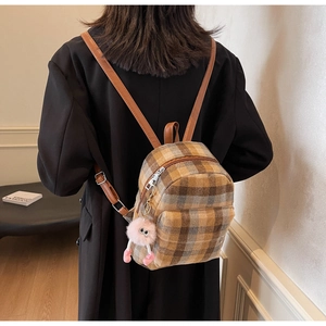 Detail of plaid backpack with plush charm worn by model in a cozy indoor setting