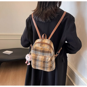 Detail of vintage plaid backpack with leather straps and a cute plush pink charm