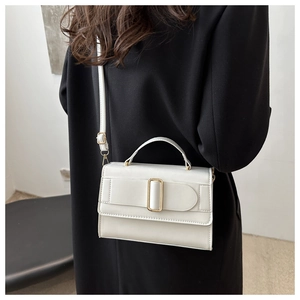 Detail of white leather handbag with gold buckle and adjustable strap worn by model