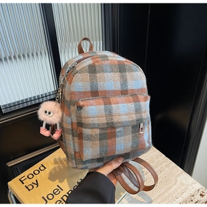Detailed view of checkered plaid mini backpack with fuzzy pink monster charm and leather straps