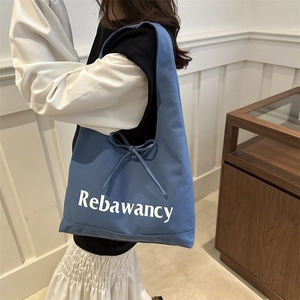 Large blue canvas tote bag with Rebawancy text and side bow detail on a model