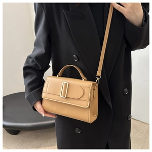 Detail of khaki square crossbody bag with gold buckle worn by model in black blazer
