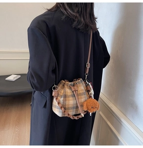 Sac seau à carreaux avec poignée en cuir et charm nounours porté par un mannequin