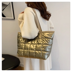 Sac fourre-tout matelassé doré métallisé porté à l'épaule dans un décor minimaliste