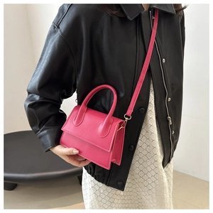 Detail of a bright pink mini leather crossbody bag with a curved handle and slim strap