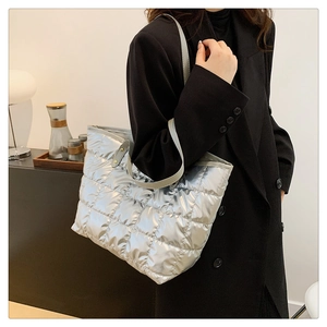 Silver quilted tote bag with diamond stitching and leather straps on model with black suit
