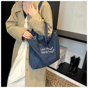 Detail of blue denim tote bag featuring white Less Mondays More Sundays embroidery