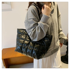 Detail of a black quilted puffer tote bag showing glossy texture and large square pattern