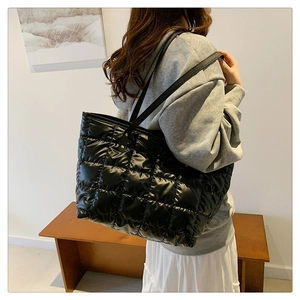 Detail of black quilted puffer tote bag with glossy finish and slim shoulder straps