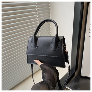 Close-up of a minimalist black leather square handbag with top handle and shoulder strap