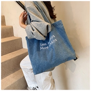 Detail of blue denim tote bag with white embroidery 'Less Mondays More Sundays' slogan