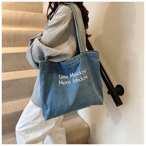 Blue denim tote bag with white embroidery lettering shown in a casual lifestyle setting