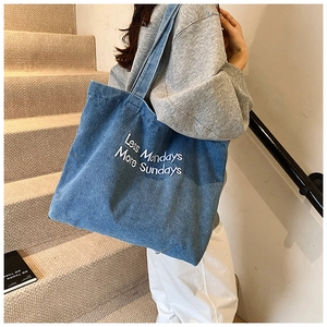 Detail of blue denim tote bag featuring white Less Mondays More Sundays embroidery