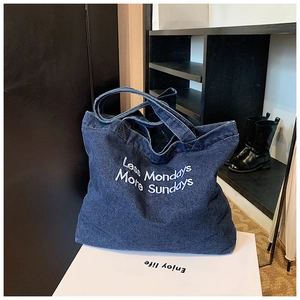 Detail of blue denim tote bag featuring white Less Mondays More Sundays embroidery