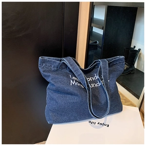 Detail of blue denim tote bag featuring white slogan embroidery and double handle design