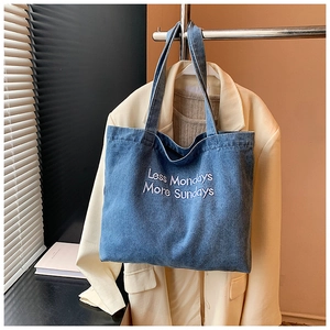 Detailed close-up of blue denim tote bag featuring purple embroidered aesthetic lettering