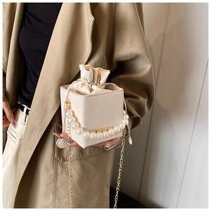 Détail d'un sac seau tissé avec poignée en perles et bandoulière en chaîne dorée