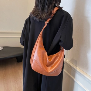 Brown faux leather hobo bag with pleated texture and adjustable strap on a shoulder