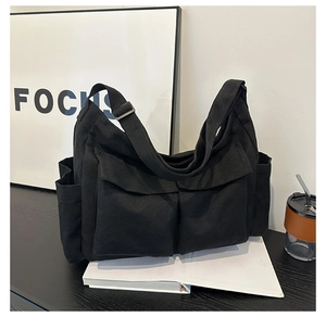 Detail of black canvas tote bag showing large front flap pockets and adjustable shoulder strap