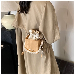 Detailed view of mini bucket bag with pearl handle and woven texture worn crossbody