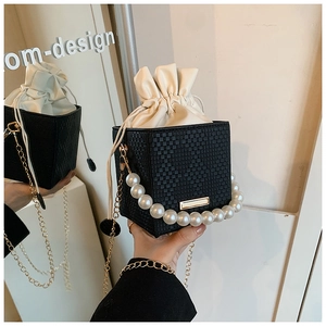 Detail of cube bucket bag featuring pearl handle and drawstring inner pouch in black and white