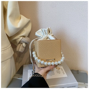 Détail du sac seau beige tressé avec poignée en perles et fine bandoulière dorée