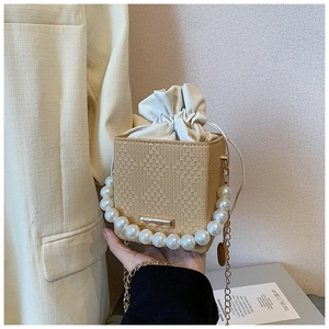 Détail du sac carré tressé beige avec anse en perles blanches et chaîne dorée
