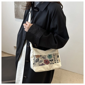 Close-up of white shoulder bag featuring colorful floral embroidery on a black coat