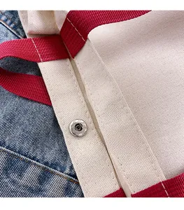 Close-up of silver magnetic clasps and red handles on a cream canvas tote bag