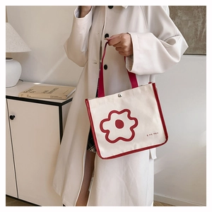 Detailed close-up of a small cream canvas handbag with red floral print and red handles