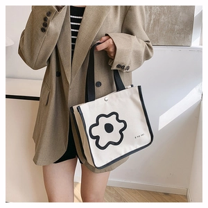 Detail of off-white canvas tote bag featuring black floral print and woven handles