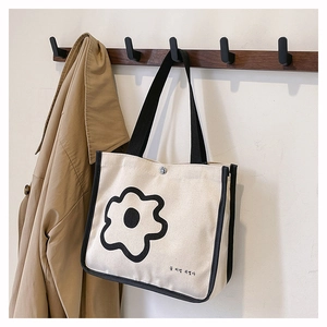 Detail view of canvas tote bag with black flower print and contrast trim on a wooden hook