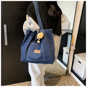 Détail du sac cabas en denim bleu foncé avec poche extérieure et écusson en cuir