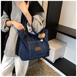 Détail du sac cabas en denim bleu avec poche avant et porte-clés animal en peluche