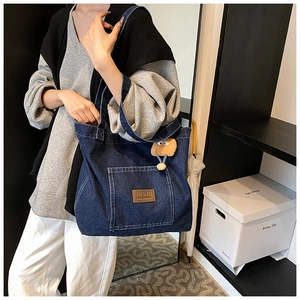 Détail d'un grand sac cabas en jean avec écusson en cuir marron et pendentif en peluche