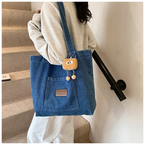 Detail of blue denim tote bag with leather logo patch and yellow plush biscuit charm