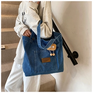 Détail du grand sac cabas en jean bleu avec étiquette cuir et breloque peluche