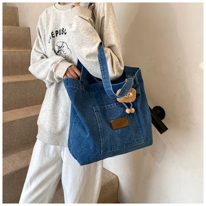 Détail du sac cabas en denim bleu avec grande poche frontale et charmant pendentif en peluche
